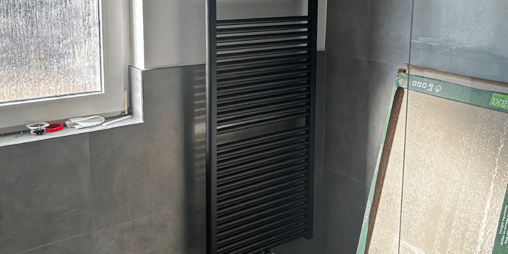Schwarzer Design-Heizkörper im modern gefliesten Bad mit Fenster und Glasdusche - Ademi Sanitär Delmenhorst - Heizung Badezimmer Klima Schwarzer Badheizkörper und moderne Fliesen von Ademi Sanitär in Delmenhorst