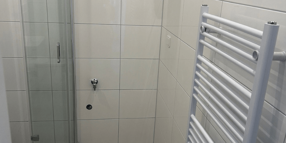 White tiled bathroom corner with a glass shower door on the left and a white heated towel rail on the right.