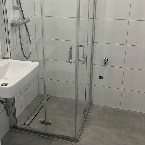 Bathroom with a glass-front shower enclosure and a wall-mounted sink to the left.